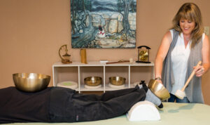 Brenda Negley holding singing bowl to feet of client